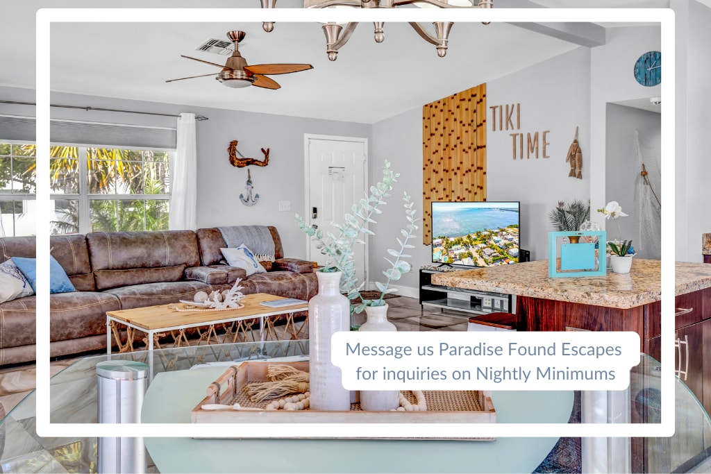 A spacious living area is presented, featuring a comfortable sectional couch facing an entertainment unit with a television. Natural light enters through large windows, highlighting a decorative coffee table and a polished kitchen island with granite countertops.