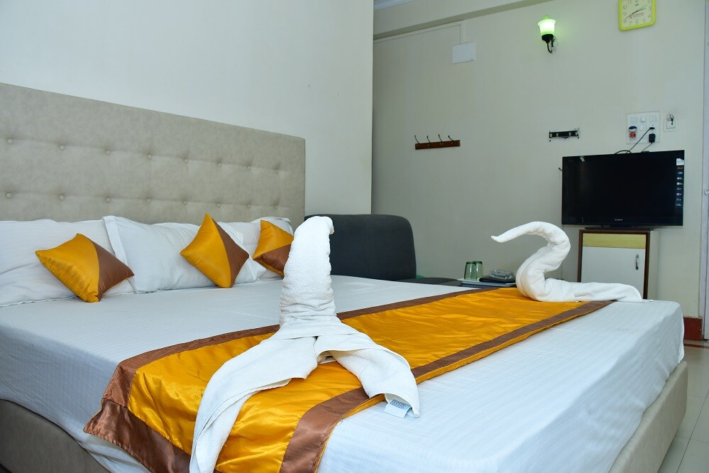 A spacious bed is dressed in crisp white linens, complemented by decorative gold and brown accents. Two swan-shaped towel arrangements are positioned on the bed. A small television is mounted on the wall, and a comfortable seating area is visible in the background.
