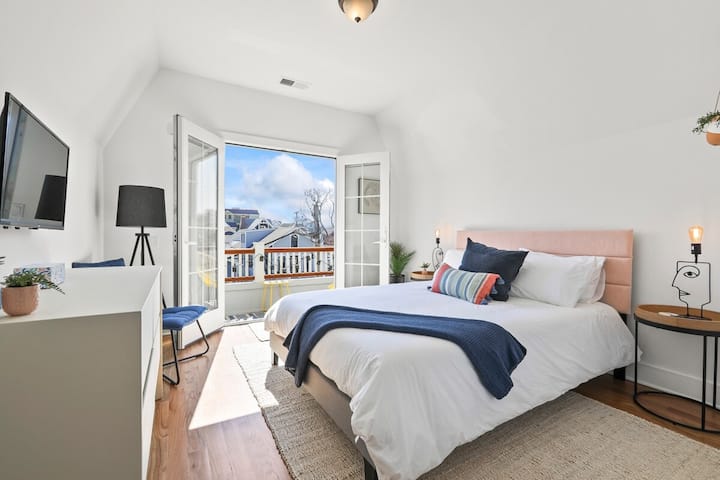 Top Floor Queen Bedroom-Wake up to natural light in this serene bedroom, featuring a comfortable bed with crisp white linens and a plush blue throw. Step outside through the French doors onto your private balcony to enjoy the neighborhood views.
