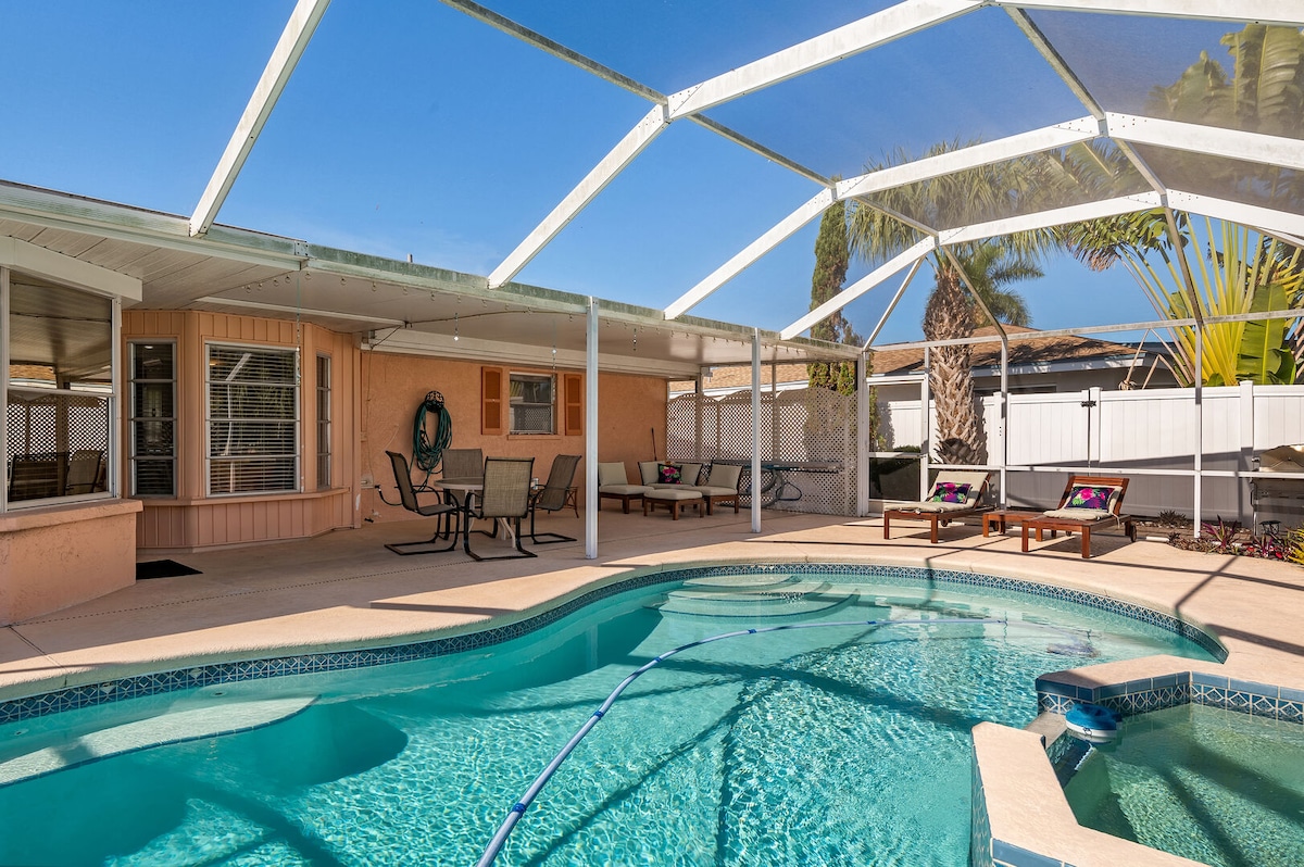 The outdoor pool area features a spacious pool surrounded by a screened lanai. Comfortable loungers and a dining set provide options for relaxation and socializing. Sunlight reflects off the water, enhancing the inviting atmosphere of this private retreat.