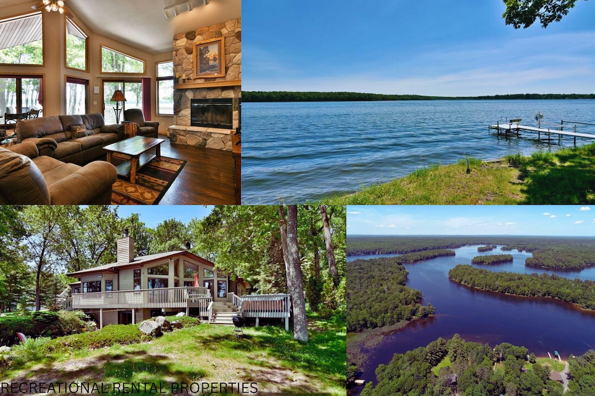 A cozy living room is presented with comfortable seating and a stone fireplace. Stunning lake views are visible outside, along with a private dock and expansive water. An aerial view highlights the property surrounded by trees, showcasing a spacious deck and serene landscape.