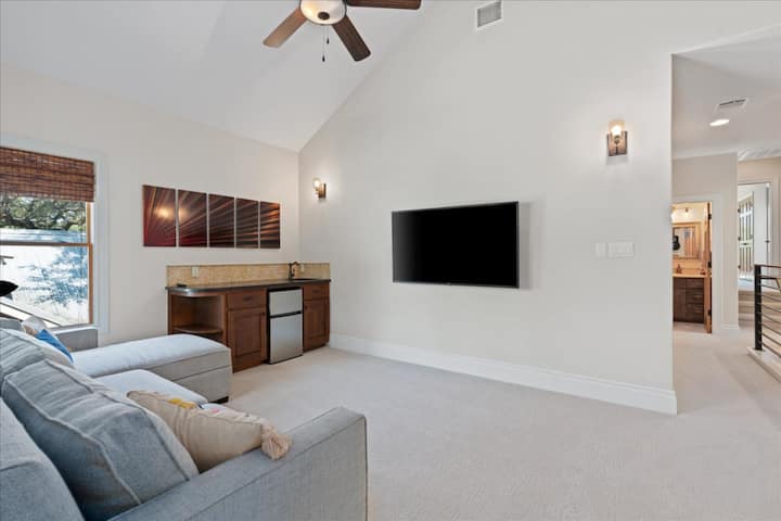 Área de estar no andar de cima com TV 4K, mini geladeira, bar molhado e sofá-cama.