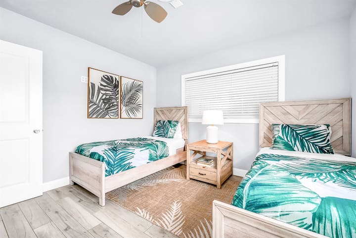 El dormitorio con dos camas individuales es ideal para niños o adultos jóvenes, con dos camas individuales en una alfombra natural. Las obras de arte tropicales realzan el ambiente de la habitación, creando un ambiente paradisíaco relajante.