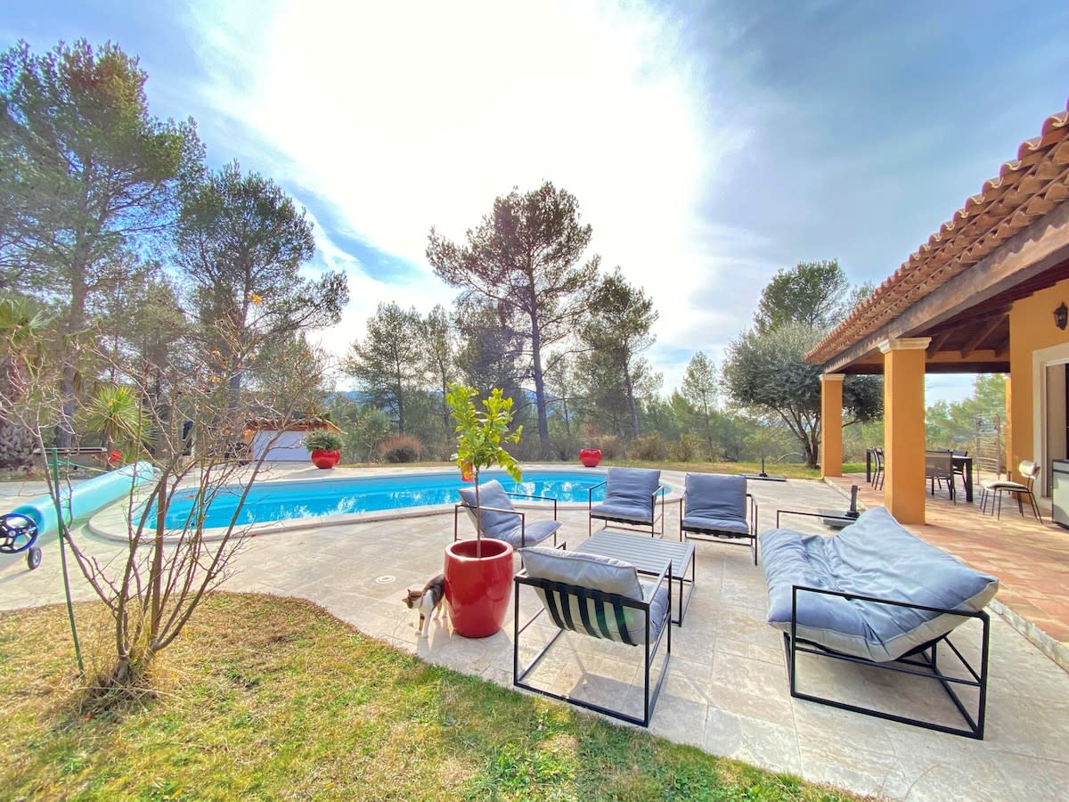 A serene outdoor space features a sparkling private pool surrounded by comfortable lounge chairs, inviting relaxation. Lush greenery and trees create a peaceful atmosphere, while a sunlit terrace offers a welcoming spot for enjoying the natural surroundings.