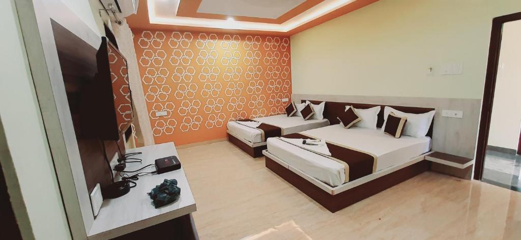 A bright guest room featuring two spacious beds, each adorned with matching dark and light pillows. A flat-screen TV is mounted on the wall opposite the beds. Colorful floral patterns create an energetic atmosphere on the accent wall, complemented by neutral furnishings and natural light from a window.