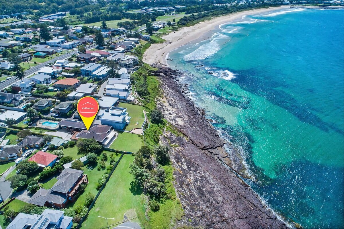 An aerial view captures the property set against the stunning coastline of Shellharbour. Clear blue waters are visible alongside sandy beaches, while the rocky shoreline adds texture to the landscape. The layout of the neighborhood reveals a mix of residential homes and proximity to the ocean.