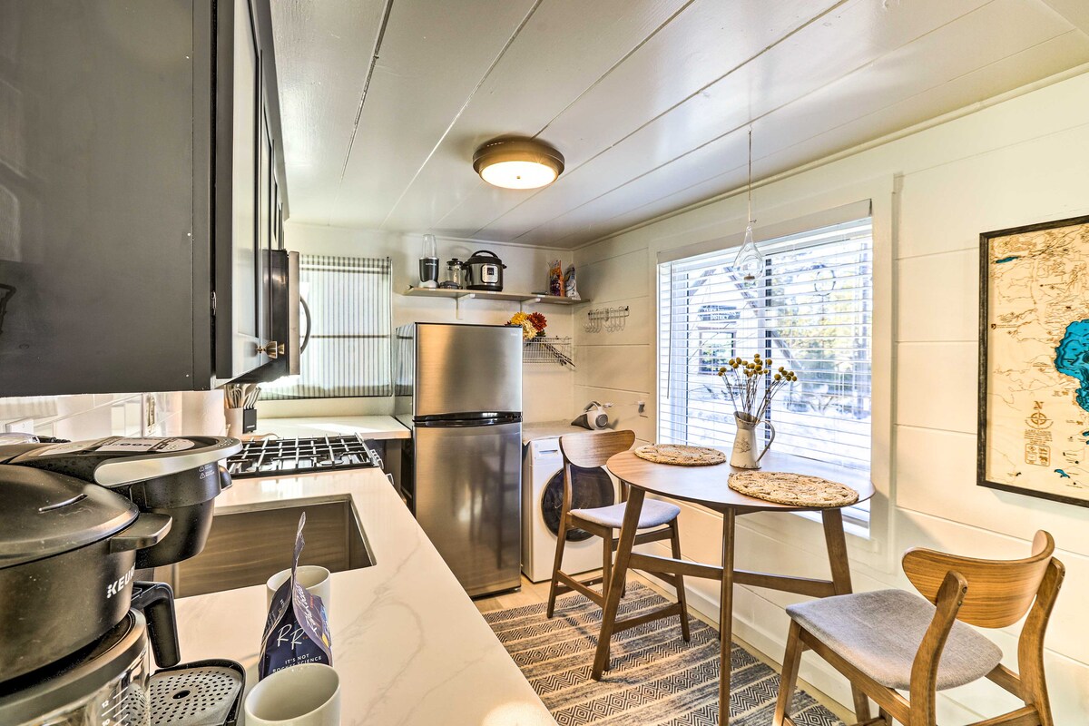 A well-equipped kitchen features sleek black cabinets and modern appliances, including a refrigerator and stove. A dining area is adorned with a round table and two wooden chairs, complemented by a window that allows natural light to fill the space.