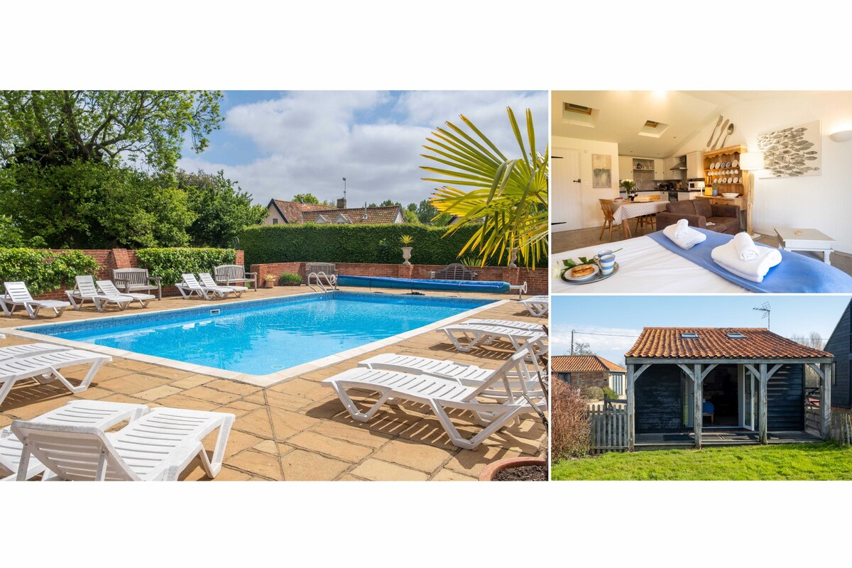 The outdoor heated swimming pool is surrounded by a spacious patio area with sun loungers. A well-maintained garden and trees provide a serene backdrop. An indoor view displays an open plan sitting area with a kitchenette, comfortable seating, and dining space, creating a welcoming gathering spot.