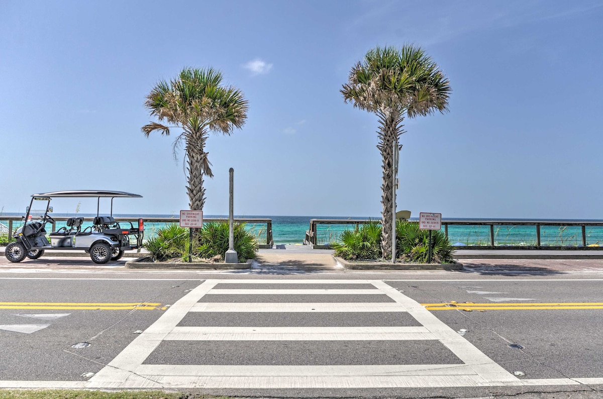A scenic view is presented, showcasing palm trees lining a pathway overlooking the ocean. A golf cart is parked nearby, with the vibrant blue water visible in the background. Clear skies enhance the coastal ambiance, creating a refreshing outdoor environment.