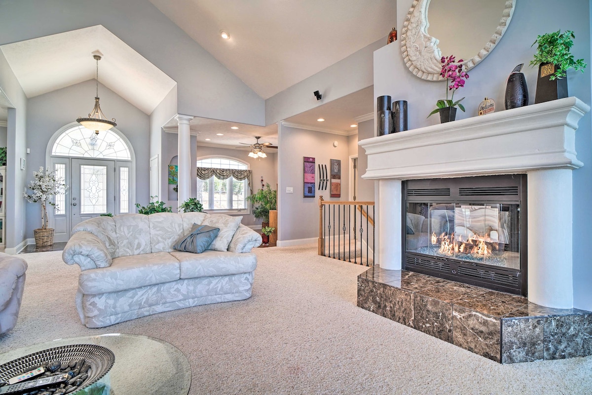A spacious living area is highlighted by a cozy fireplace set within a stone mantle. Natural light floods the room through large front windows, while a plush sofa with decorative pillows invites relaxation. The neutral decor and subtle floral accents add a soothing touch.