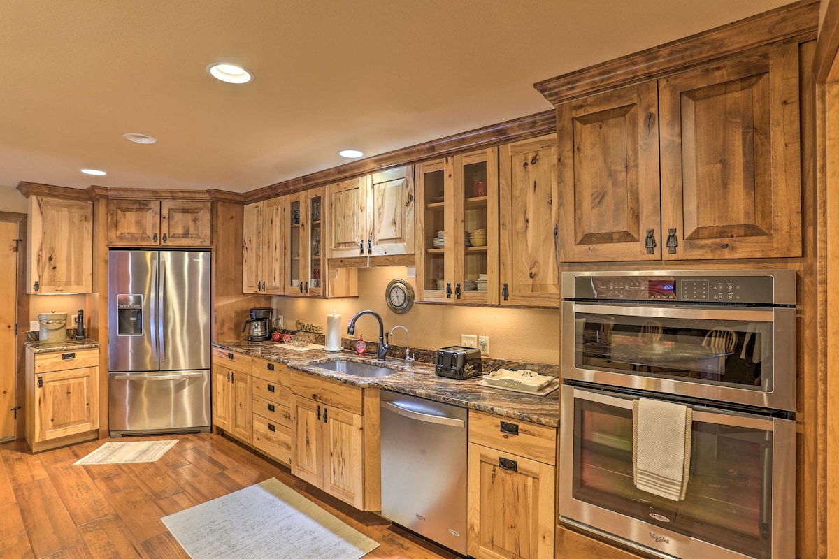 The kitchen features natural wood cabinetry with glass-front doors, stainless steel appliances, and a granite countertop. Under-cabinet lighting illuminates the workspace. A white area rug is positioned in front of the sink, creating a comfortable and functional cooking area.