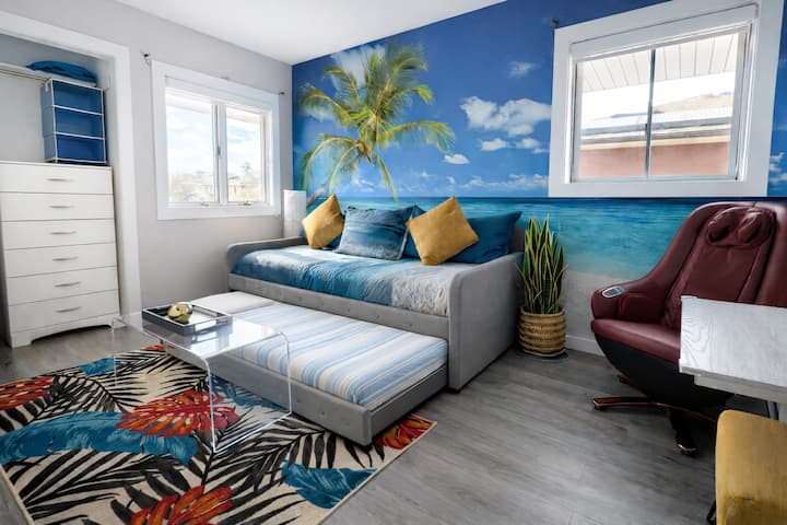 טרקלין חוף שטוף שמש עם ציור קיר של ים, ספה נפתחת, שולחן וכורסה נפתחת.