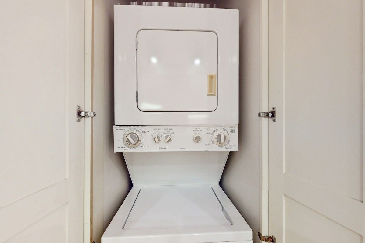 A stacked washer and dryer unit is neatly enclosed in a cabinet, featuring a white exterior. The control panel includes dials and settings for both washing and drying functions. The cabinetry offers a clean and organized appearance.