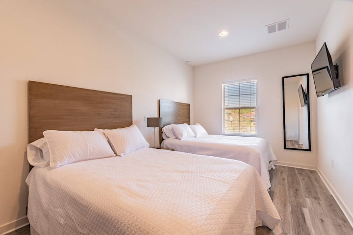 Disfruta de noches tranquilas en este encantador dormitorio con dos camas acogedoras vestidas con sábanas blancas y frescas, una luz natural acogedora, un elegante espejo de cuerpo entero y un televisor elegante para ayudarte a relajarte después de las aventuras del día.
