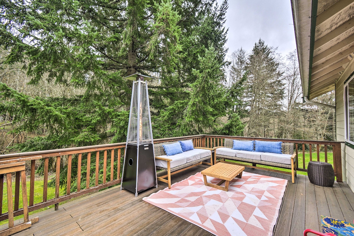 A furnished deck features a stylish outdoor seating area with a coffee table and soft cushions on sofas. A patio heater stands tall nearby, surrounded by greenery that enhances the natural setting of the property.