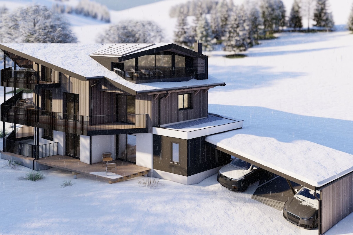 A stylish mountain building surrounded by snow-covered terrain is shown. The structure features multiple balconies and a carport accommodating two vehicles. Trees scattered in the background enhance the serene winter landscape, while gentle slopes are visible beyond the property.