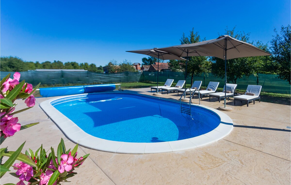 A private outdoor swimming pool is surrounded by shaded loungers and lush greenery. The pool features a clear, inviting water surface, while sun umbrellas provide relief from the heat. Colorful flowers in the foreground enhance the tranquil setting.
