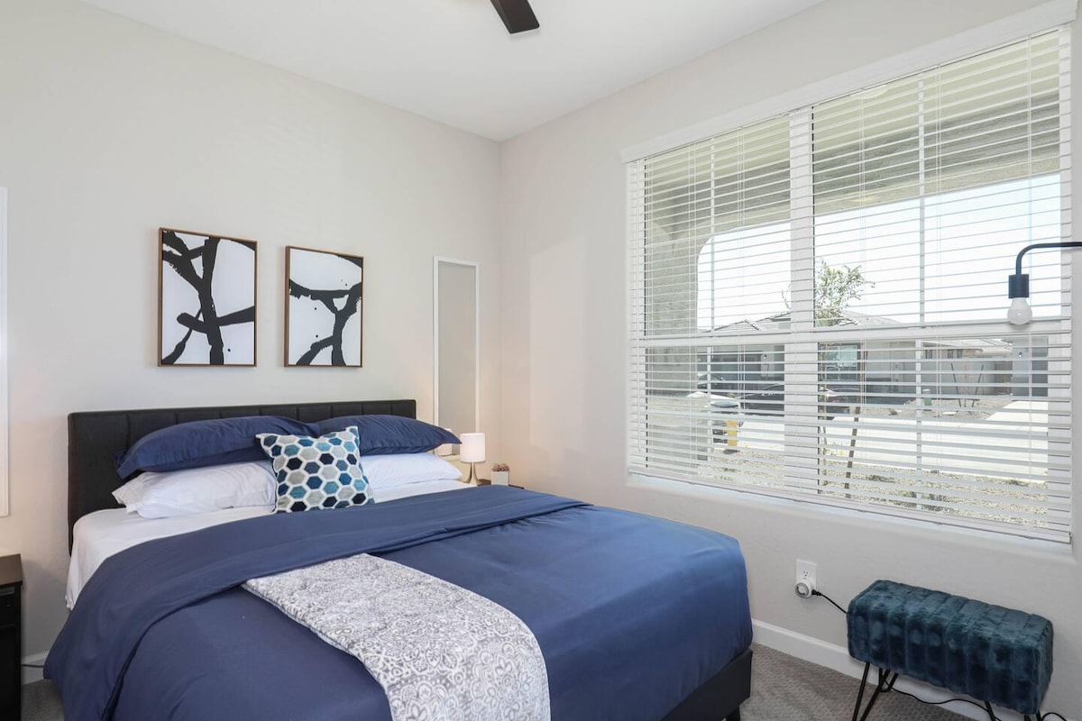 Светла и привлечна гостинска спална соба со брачен кревет, стилски декор и големи прозорци за многу природна светлина.