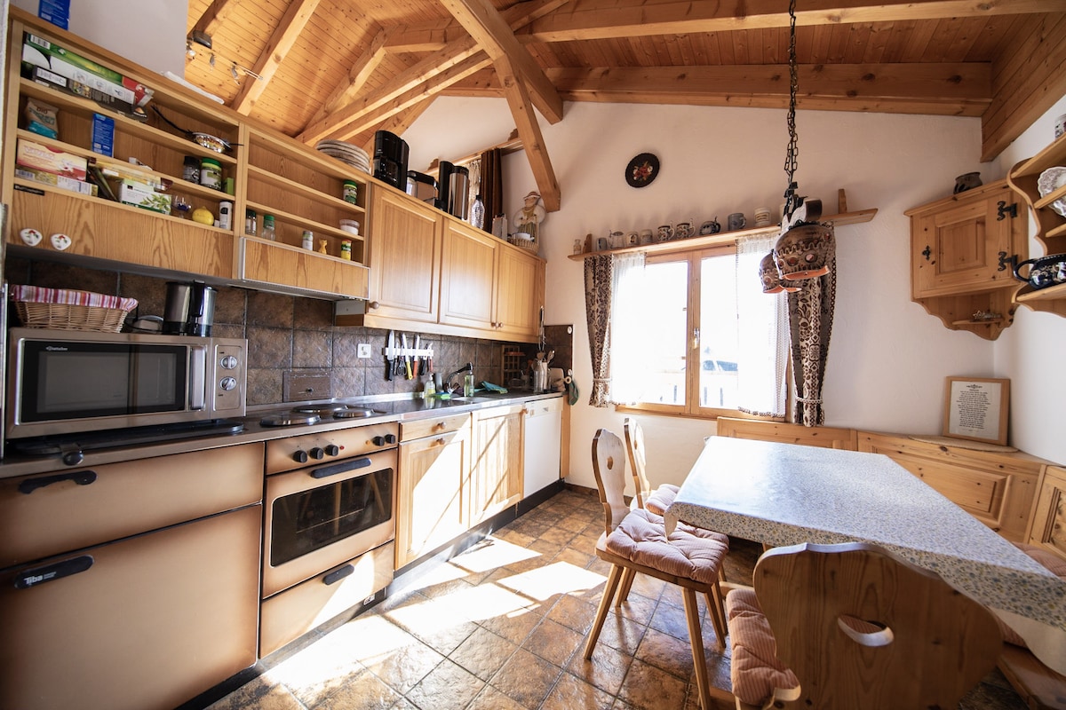 A well-equipped kitchen features wooden cabinetry and a stone-topped countertop. A microwave and oven are situated alongside a stove. Natural light enters through a large window above the sink, illuminating the dining area with a table and several chairs, enhancing the homey atmosphere.