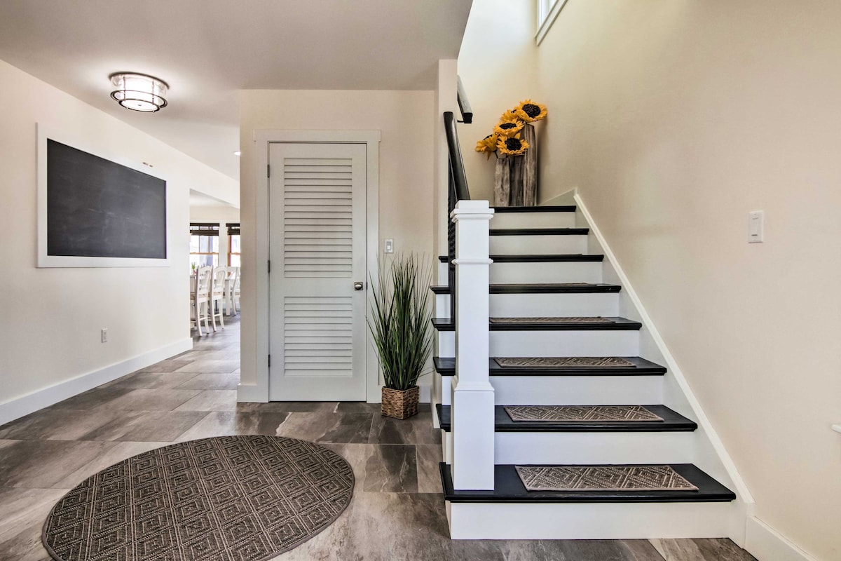 An open entryway showcases a staircase with dark wooden steps, leading to a well-lit upper level. A decorative round rug lies on the tiled floor, complemented by indoor plants and a subtle chalkboard feature on the wall.