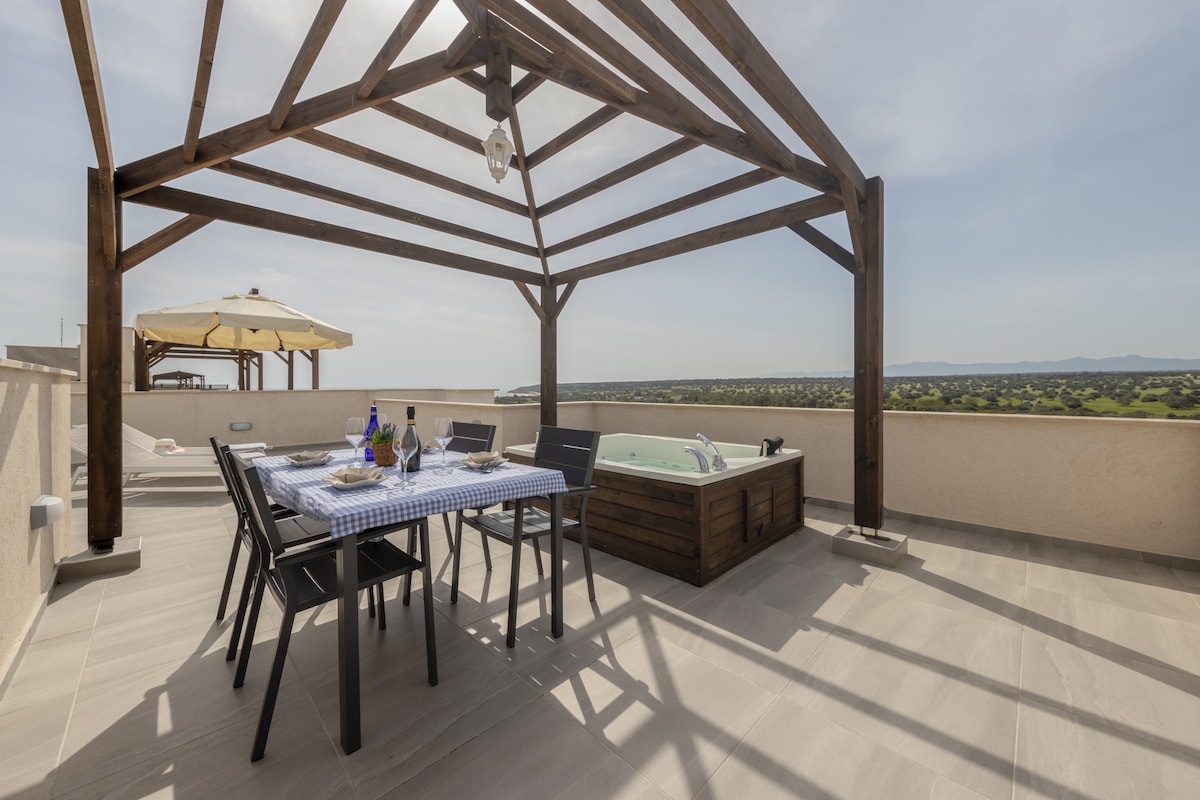 A private rooftop terrace is presented, featuring a wooden pergola with a dining table set, complemented by black chairs. A spa tub is visible, with scenic views extending beyond. A large umbrella offers shade, creating an inviting space for relaxation and dining.