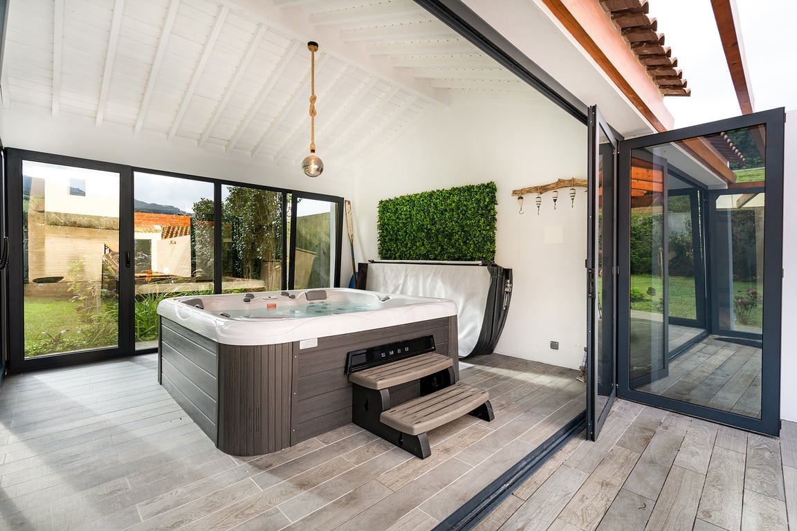 A spacious indoor area features a jacuzzi, surrounded by large glass doors that provide views of the garden. Natural light fills the space, complemented by a vertical garden panel on one wall. The modern design includes wooden flooring and subtle lighting fixtures.