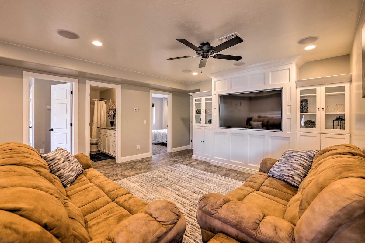A spacious living area is furnished with two comfortable couches facing each other. A ceiling fan offers circulation, while built-in cabinets and a large wall-mounted TV add functionality. Doorways lead to other areas, with natural light coming from windows covered by sheer treatments.