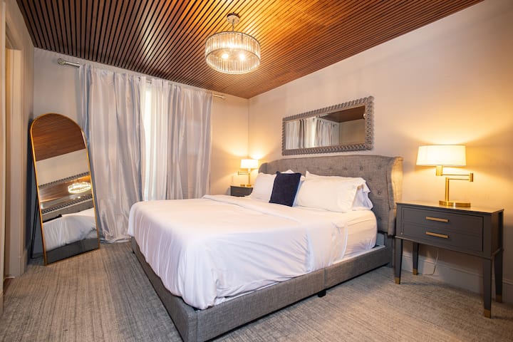 Elegante dormitorio con texturas en capas, cortinas opacas e iluminación ambiental, un refugio tranquilo para estancias largas.