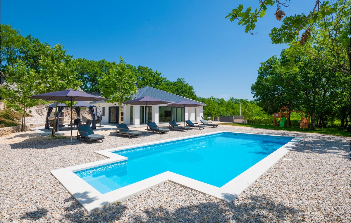 An outdoor area features a saltwater pool with a crystal-clear surface surrounded by lounge chairs and shaded by umbrellas. The property is set among lush greenery, offering a serene atmosphere. A play structure is visible in the background.
