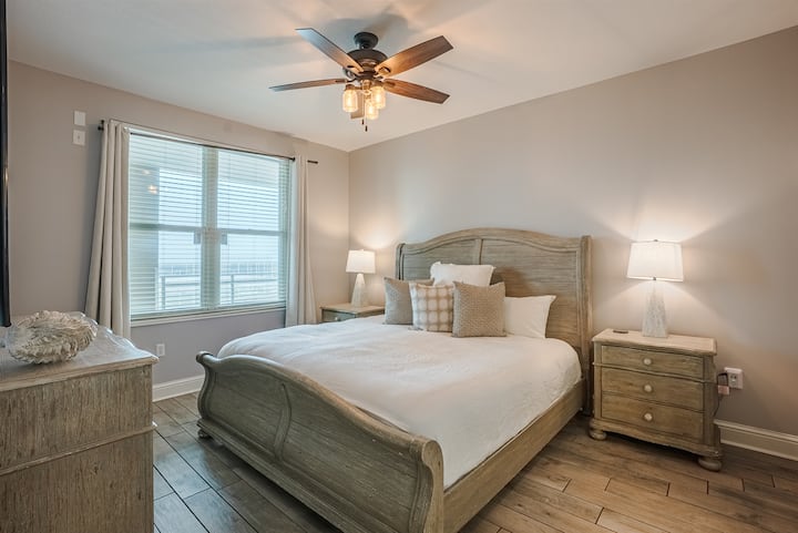 Mater bedroom with soft bedding, ceiling fan, and simple coastal touches.