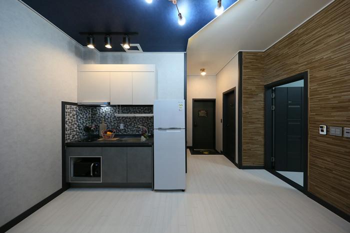 A modern kitchen area is showcased, featuring white cabinetry, a sleek refrigerator, and a dark countertop. A stylish backsplash of patterned tiles is displayed behind the sink. Adequate lighting is provided by overhead fixtures, illuminating the space. The open layout allows for ease of movement.