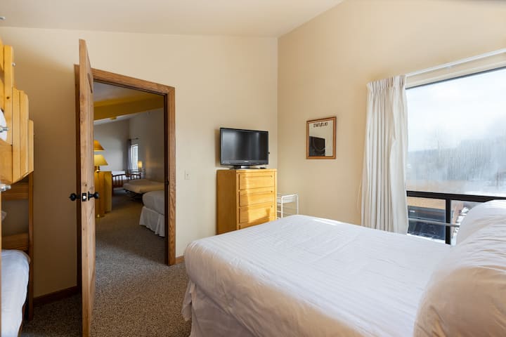 Chumba cha kulala cha roshani kilicho na kitanda cha ukubwa wa malkia, kitanda cha ghorofa mbili na televisheni ya skrini tambarare.