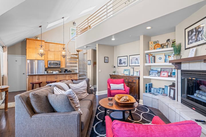 Un salón acogedor y ecléctico con una cocina abierta y un altillo con una escalera de caracol, decorado con sillones de color rosa vibrante. (40B)