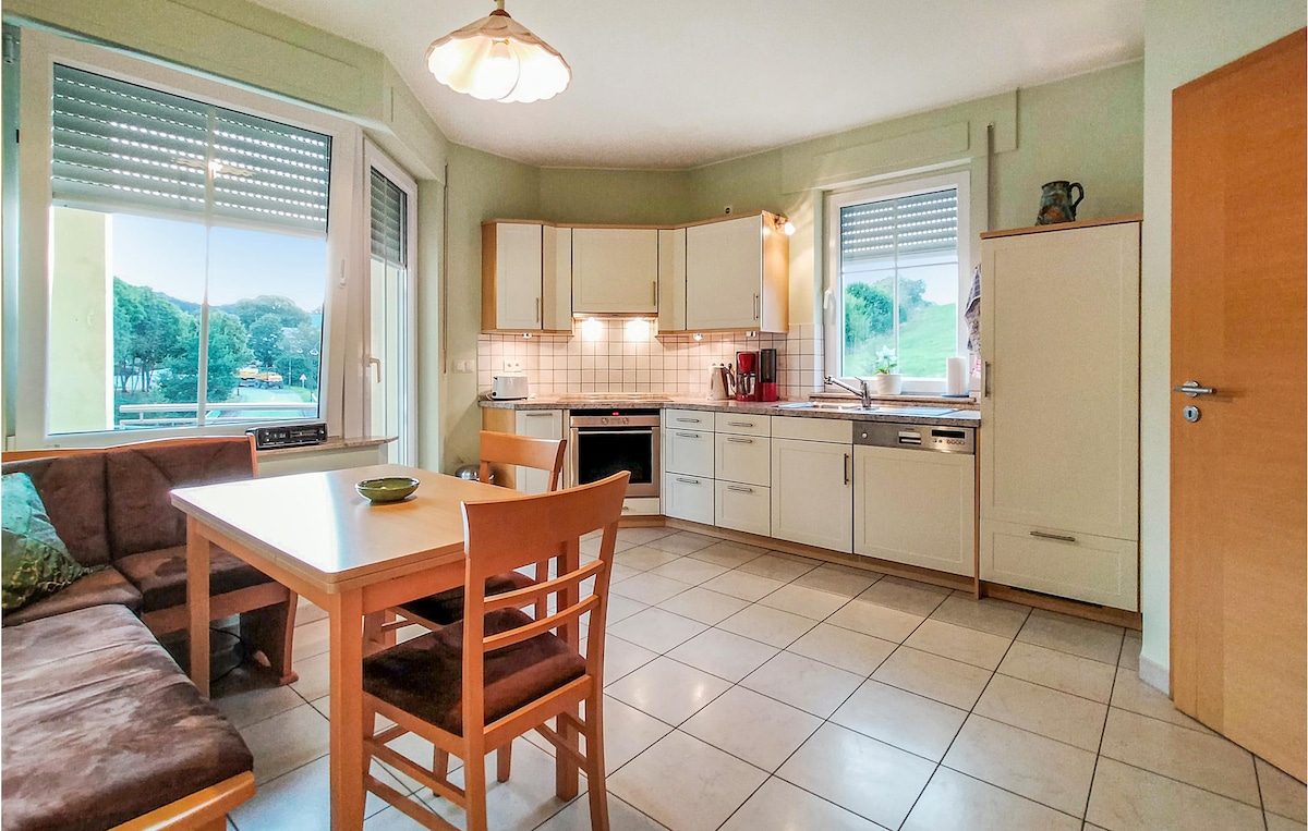 An airy kitchen and dining area features a wooden table surrounded by four chairs. Light-colored cabinets provide ample storage, with a counter space that includes modern appliances. A large window offers views of the outdoors, allowing natural light to fill the room.
