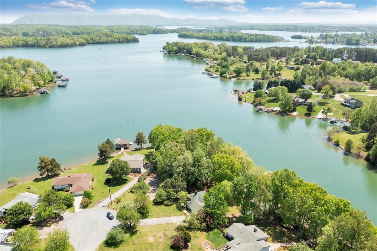 Aerial view showcasing the expansive lake surrounded by lush greenery and residential homes. The private dock of the rental property is visible along with well-maintained lawns. The tranquil water reflects the clear sky, enhancing the serene atmosphere of the lakefront location.
