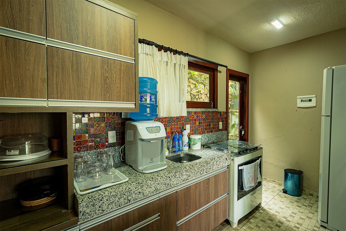 A functional kitchen showcases wooden cabinetry with a textured surface. A colorful backsplash is visible along the counter, and essential appliances, including a stove and refrigerator, are present. Natural light enters through a window, adding a welcoming touch to the space.