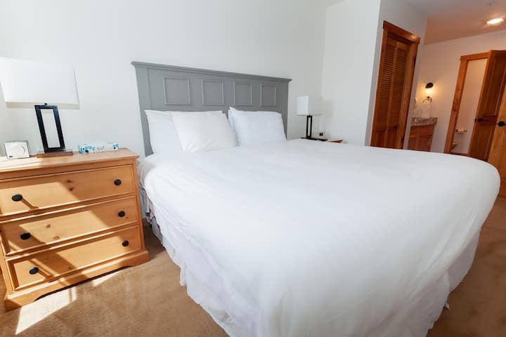 The primary bedroom features a king-sized bed and a mounted flat screen TV.