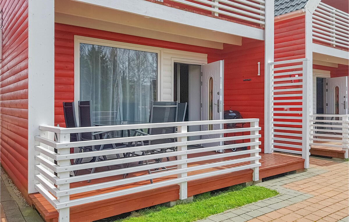 A welcoming outdoor terrace is visible, featuring a set of black chairs arranged around a wooden table. The bright red exterior of the wooden house complements the white railings and doors, creating an inviting space for relaxation.