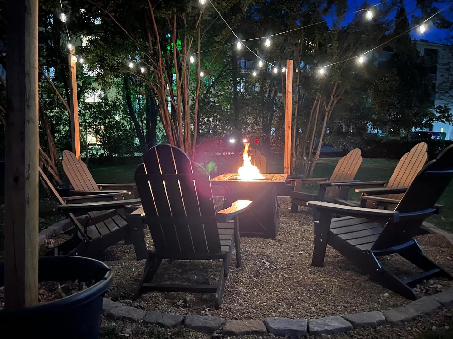 Fire pit at dusk with Adirondack chairs and string lights in the trees