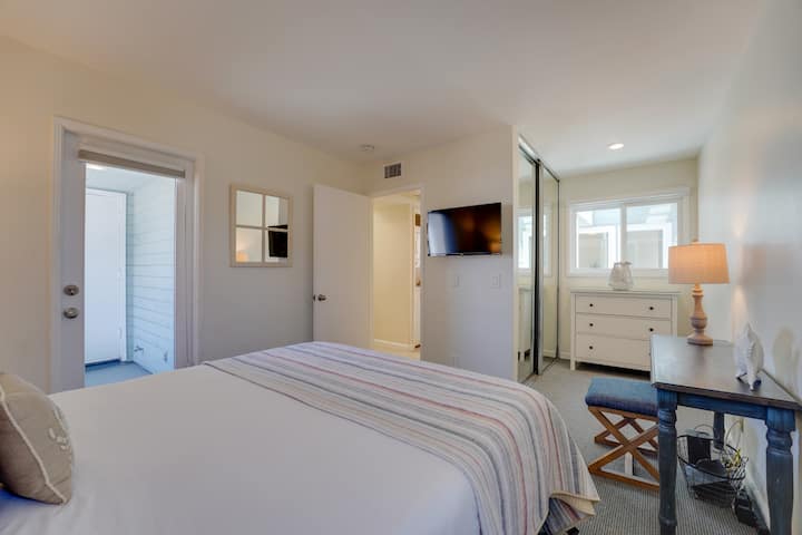 Relax in this serene bedroom retreat featuring cozy bedding, natural light, Roku TV, and beachy décor for the perfect night’s sleep.