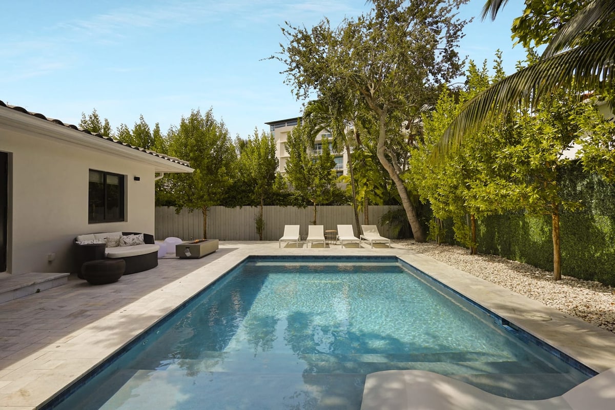 A refreshing saltwater pool invites relaxation, surrounded by well-maintained landscaping. Four lounge chairs are positioned poolside, complemented by a shaded seating area. The exterior features a tranquil ambiance with lush greenery and a fenced backyard, ensuring privacy and comfort.
