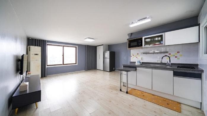 A spacious kitchen area is visible, featuring modern appliances including a refrigerator and microwave. A large window allows natural light to fill the space. A countertop with a sink and a small seating area contribute to a functional layout, complemented by light-colored flooring.