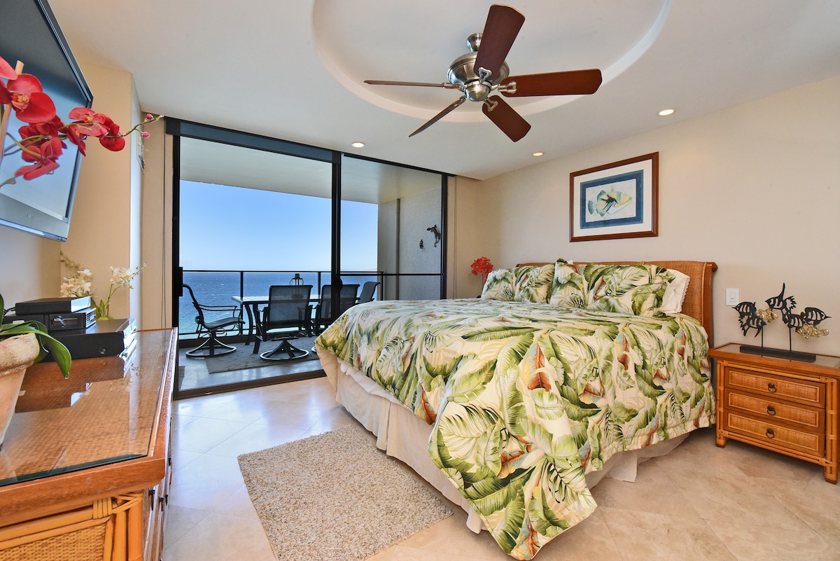Chambre lumineuse avec literie tropicale, ventilateur de plafond et vue directe sur l'océan.