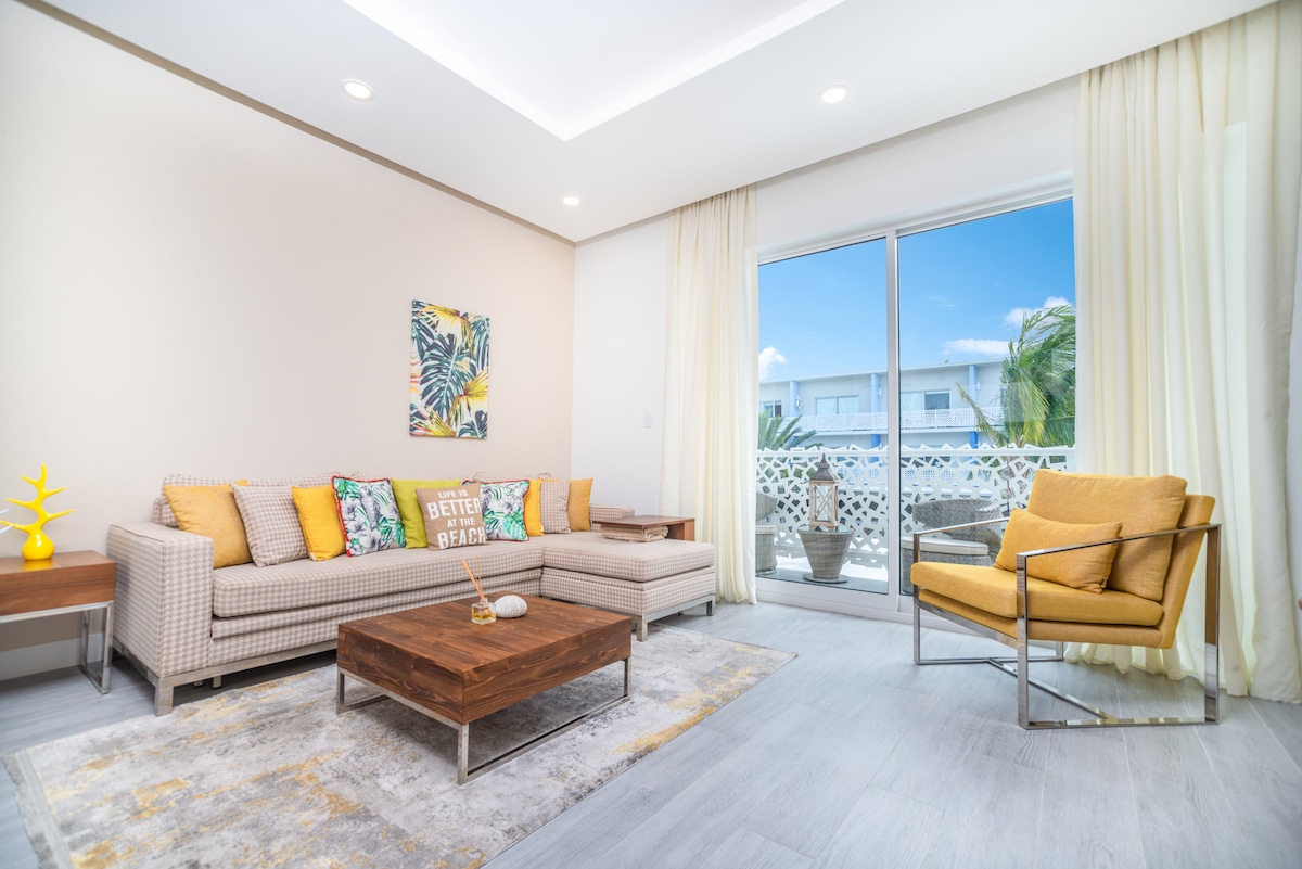 The open plan living area features a comfortable sofa adorned with decorative cushions, complemented by a bright armchair. A wooden coffee table sits on a soft rug, while floor-to-ceiling sliding doors lead to a private balcony, allowing natural light to fill the space.
