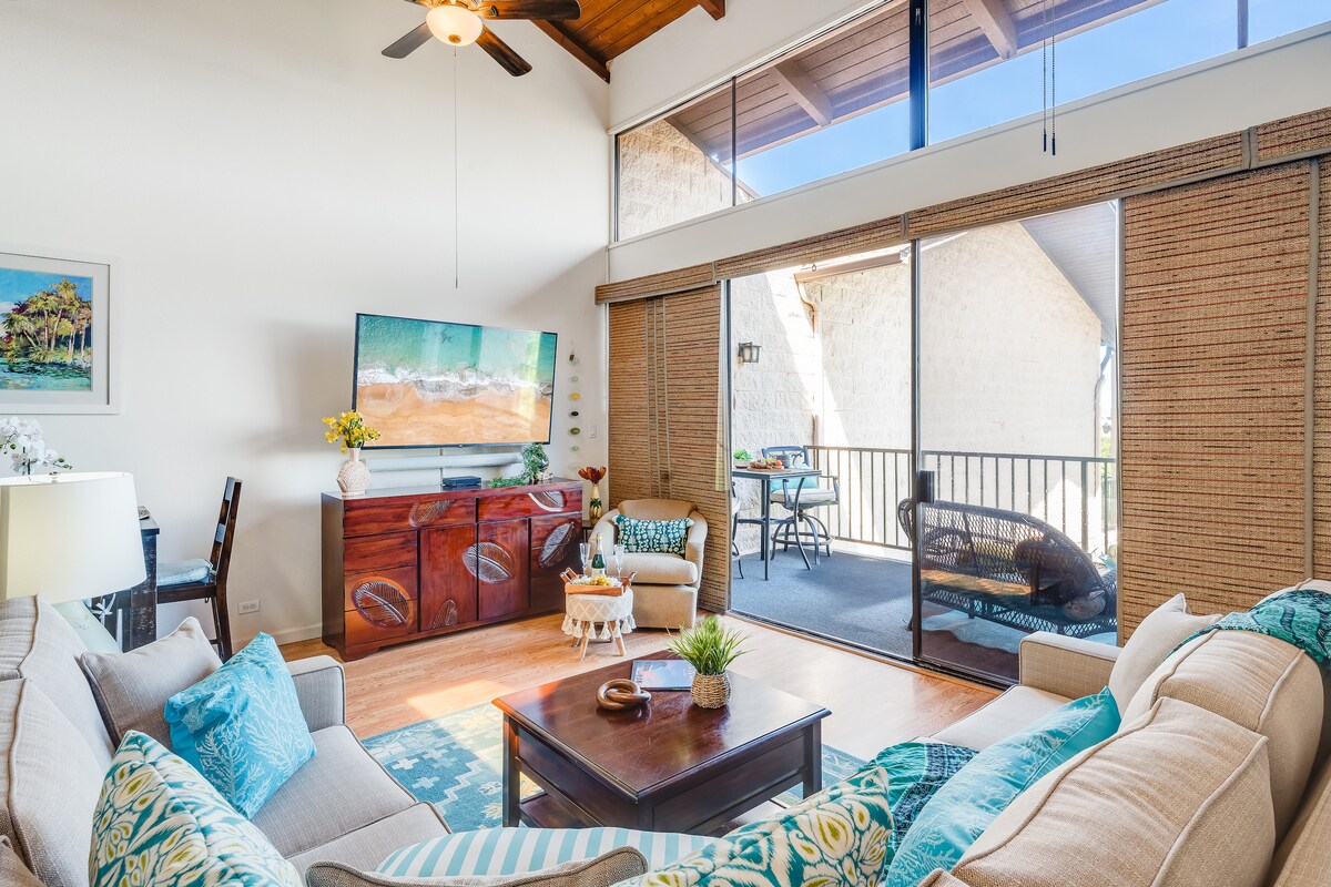 An inviting living area features a spacious sectional sofa adorned with colorful cushions, complemented by a wooden coffee table. A large smart TV is positioned against a wall, with natural light streaming through sliding glass doors that lead to a lanai with outdoor seating.