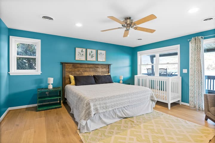 Очарователна спалня с детско креватче за малки деца, уютно легло, украсено с чисто спално бельо, успокояващ вентилатор на тавана, самостоятелен балкон, скрин за съхранение, единичен диван за допълнителен комфорт, лампа за меко осветление и нощно шкафче за удобство.