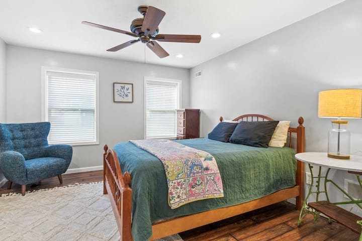 Привлекателна спалня с плюшено и удобно легло, успокояващ вентилатор на тавана, прозорци с живописни гледки, удобно нощно шкафче и меко осветена лампа за уютна обстановка .“