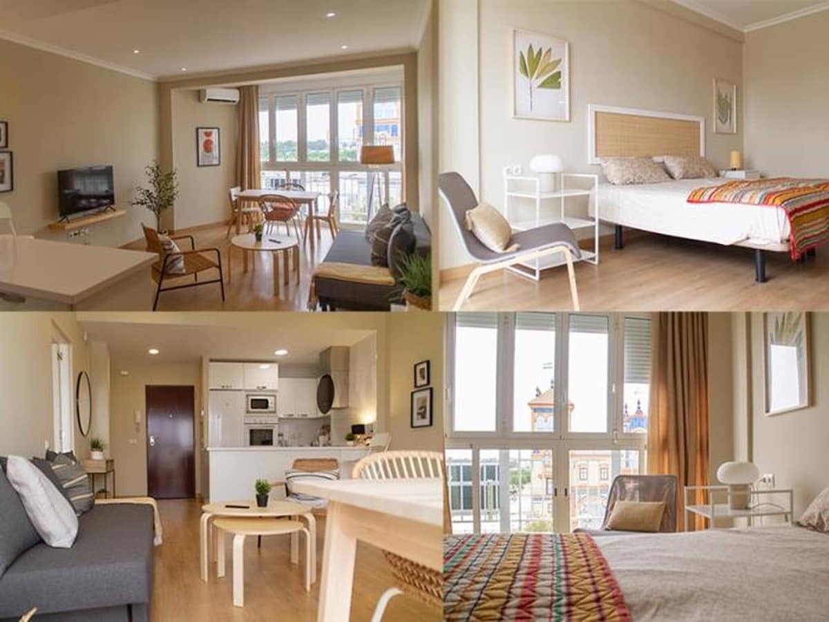 The apartment features a harmonious layout with distinct areas for relaxation and dining. Large windows allow natural light to fill the spaces, highlighting a cozy seating arrangement, a spacious bed with colorful accents, and a well-equipped kitchenette. Light wood flooring enhances the bright atmosphere.