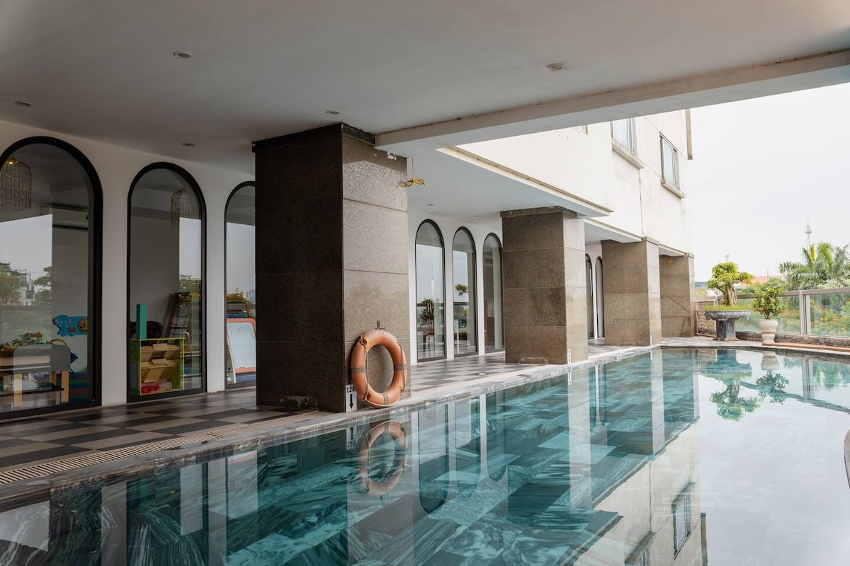An inviting swimming pool is framed by elegant arches and stylish stone columns. The pool's smooth surface reflects the surrounding area, creating a serene atmosphere. A life ring is positioned nearby for safety, adding practicality to the aesthetic appeal of the space.