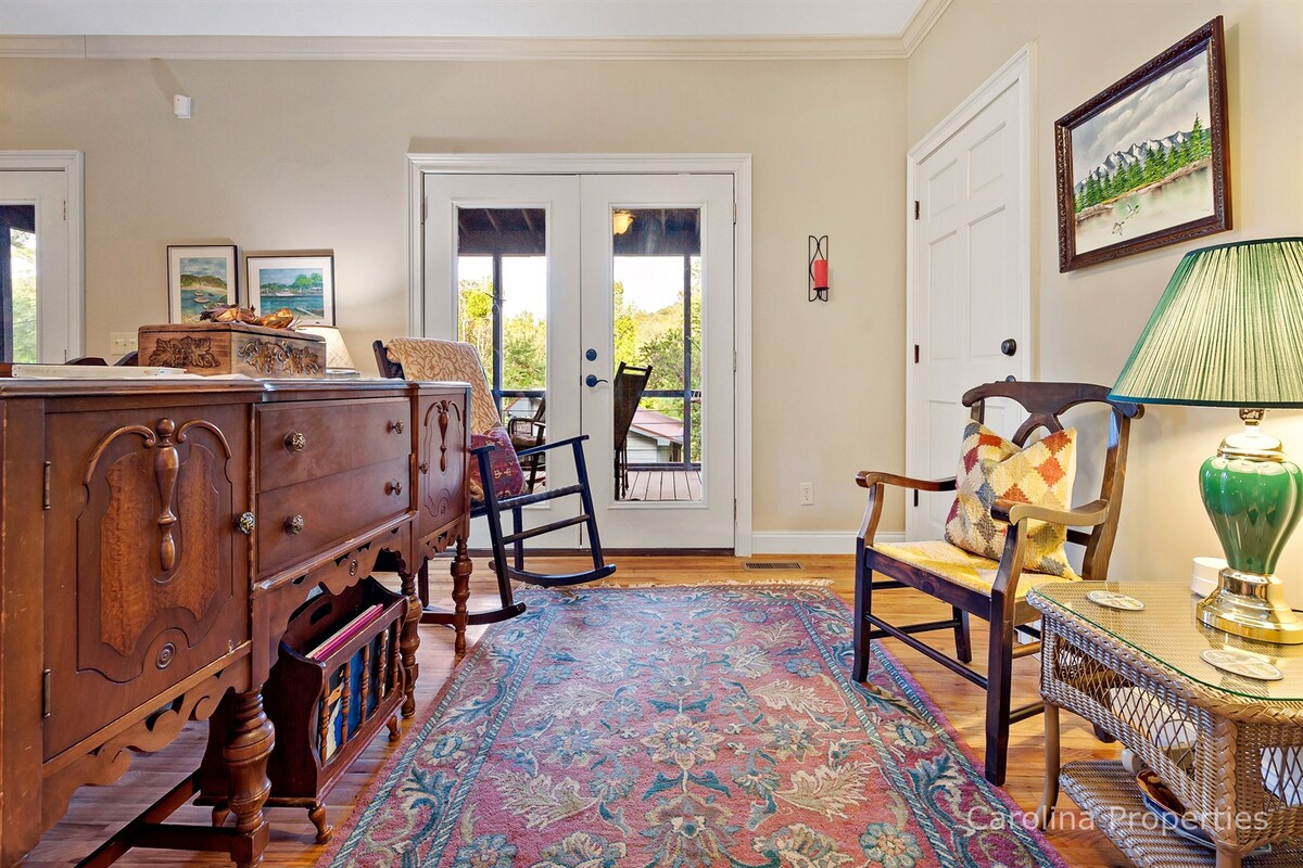 A warm entryway features a decorative wooden sideboard and a comfortable rocking chair, creating an inviting atmosphere. A vibrant area rug adorns the wooden floor, while double glass doors provide access to the outdoors, enhancing the connection between indoor and outdoor spaces.
